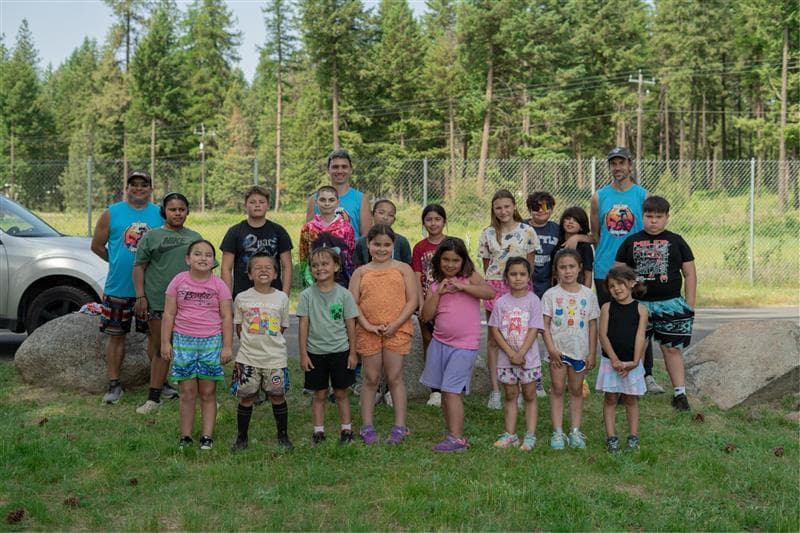 Youth runners and coaches standing together in a pine clearing at a Sko run camp.